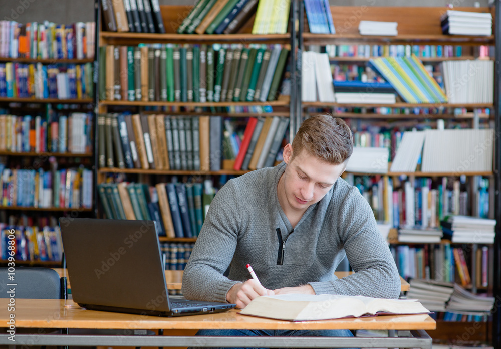 Male student with laptop studying in the university library Male student with laptop studying in the university library