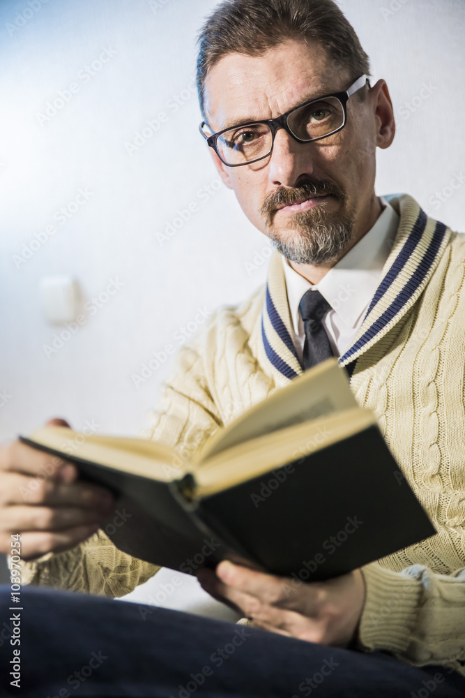a grown man reading book sitting and looking at the viewer in the camera a grown man reading book sitting and looking at the viewer in the camera