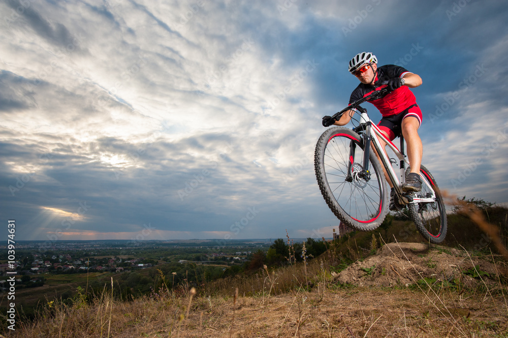 Fototapeta premium Male mountain biker jumping against blue evening sky. Low angle portrait. Extrem sport downhill cyclist