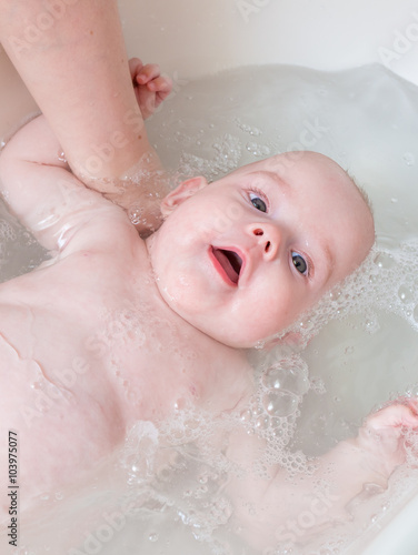 Bathing baby in bath with water. Baby care concept.