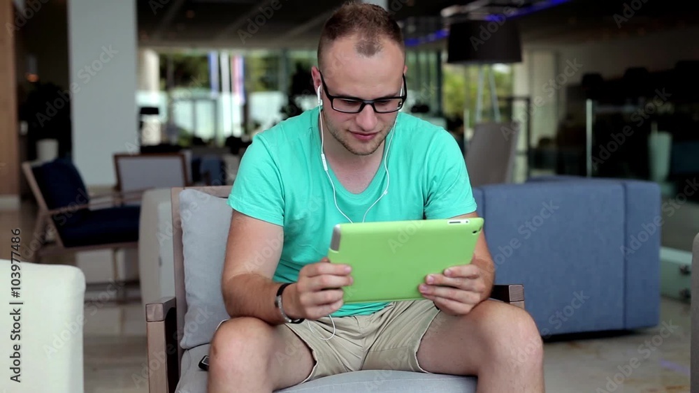 Young man writing a message on tablet from hotel lobby. Young man writing a message on tablet from hotel lobby.