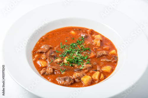 Tomato soup with meat, potatoes, carrots, parsternak in white plate. 