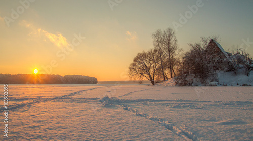 sunrise,frozen lake, reeds and old house.Footprints in the snow.