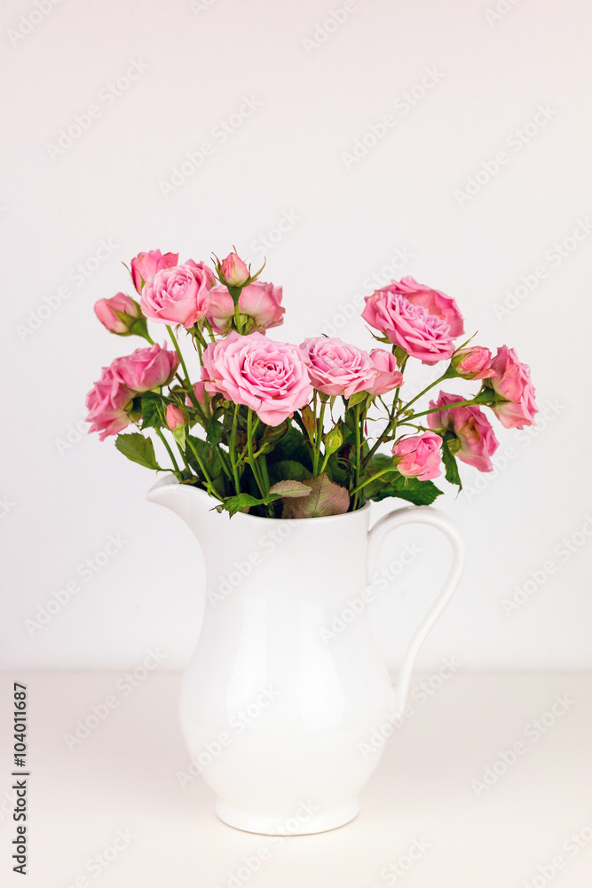 Pink flowers in white jug. Roses in jug.
