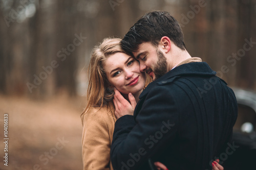 Romantic fairytale wedding couple kissing and embracing in pine forest near retro car.