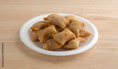 Bite size pepperoni pizza rolls on a white foam plate atop a wood table top.