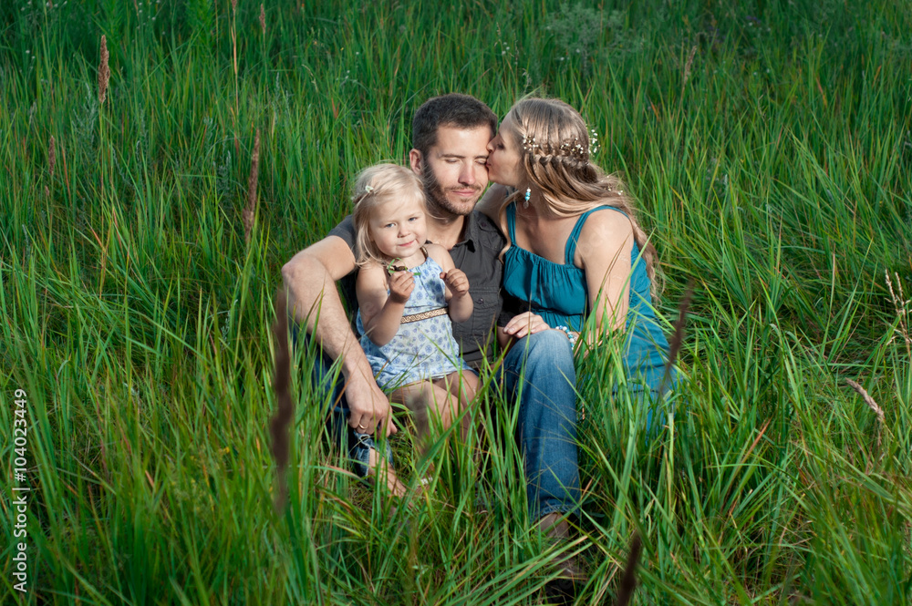 Fototapeta premium Happy family. Mother and daughter kissing daddy outdoors