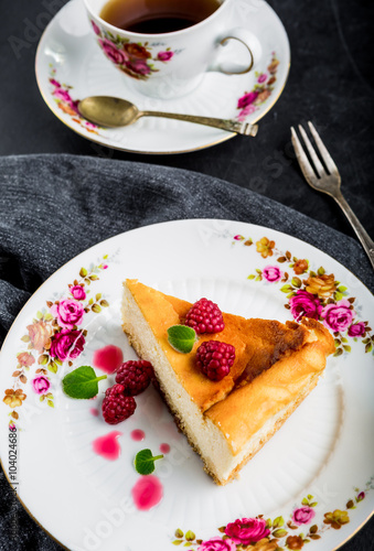 Cheesecake slice with raspberries and mint leaves on plate.