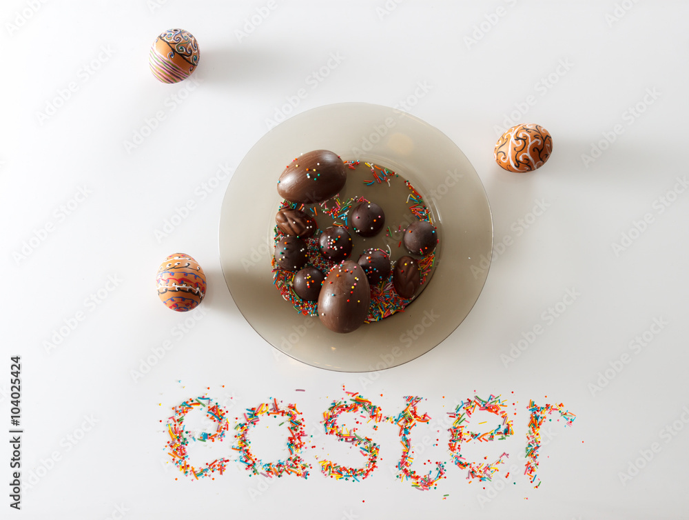 Easter made from raisins and colorful baking sugar over white background with a plate full of chocolate eggs and candies and two hand drawn eggs