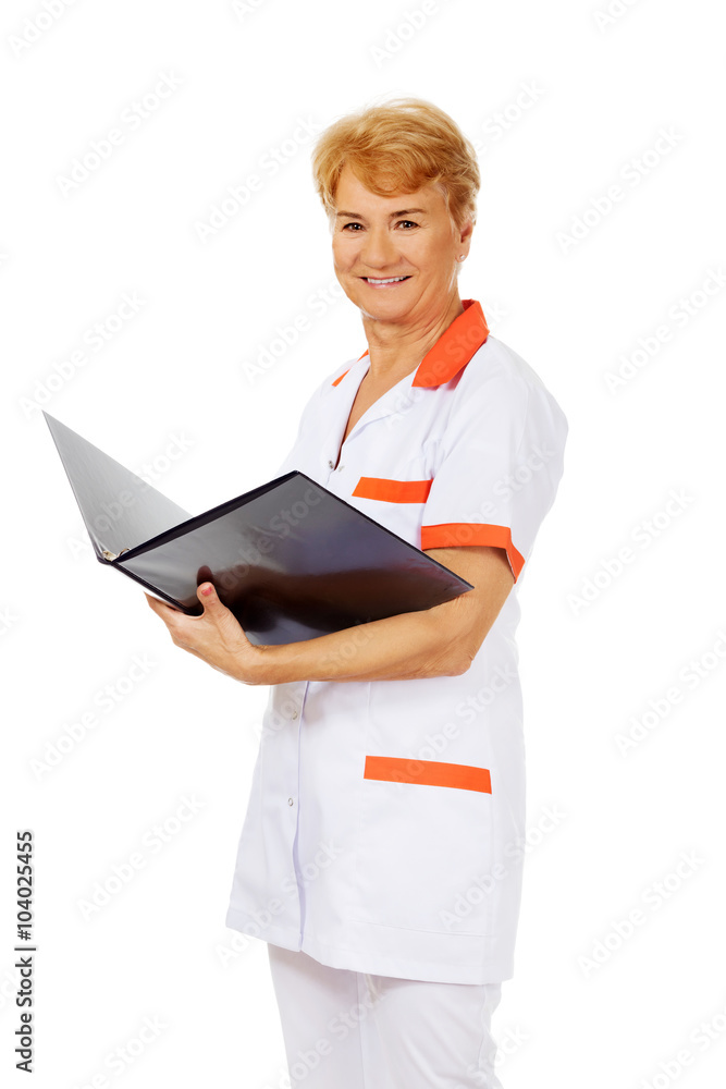 Elderly female doctor or nurse holds black binder and reads Elderly female doctor or nurse holds black binder and reads