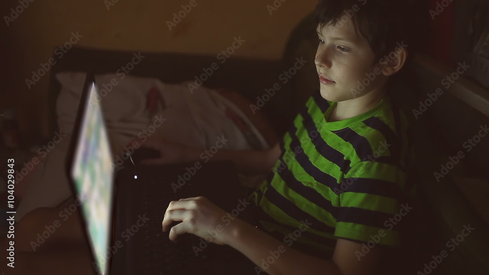 boy indoor teen with laptop computer plays game on Internet boy indoor teen with laptop computer plays game on Internet