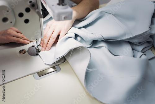 seamstress sews clothes and put thread in needle. Workplace of tailor - sewing machine, rolls of of thread, fabric, scissors.