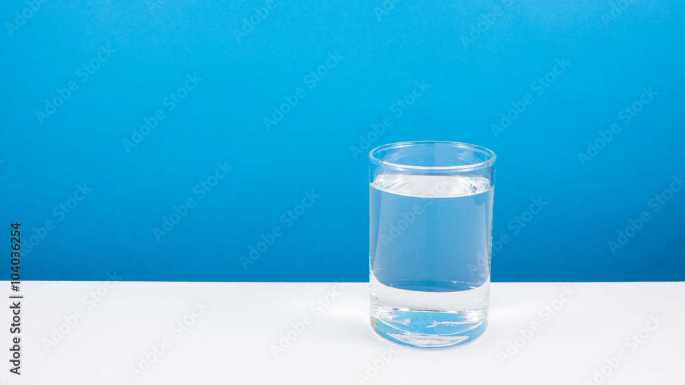 The medium cylinder glass of pure mineral water on a white table.