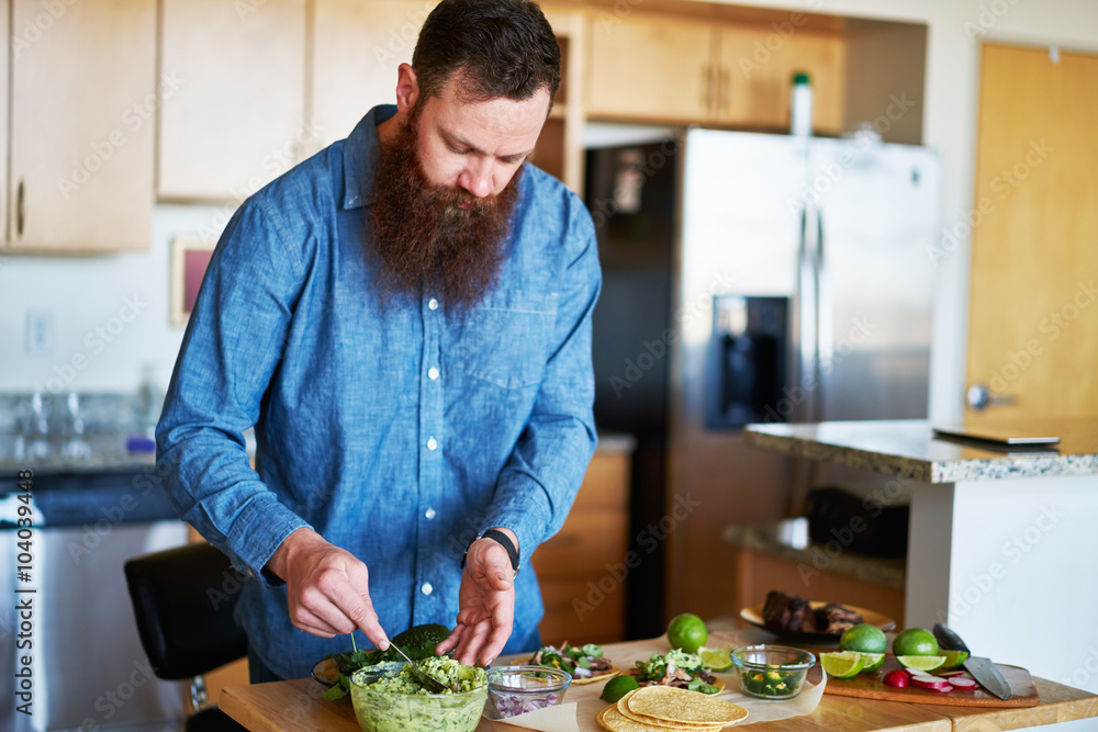 hipster guy with beard tasting homemade guacamole in kitchen hipster guy with beard tasting homemade guacamole in kitchen