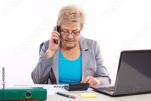 Elderly business woman talking on mobile phone and working at her desk in office, business concept