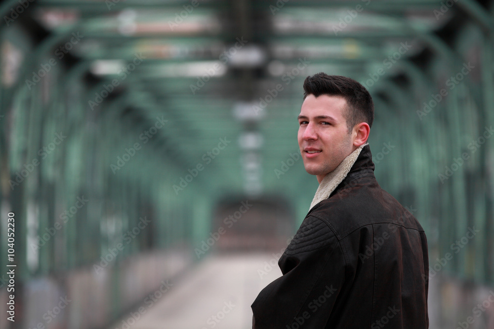 Attractive young man wearing leather jacket looking back over his shoulder Attractive young man wearing leather jacket looking back over his shoulder