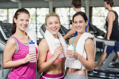 Athletic smiling women posing with bottle of water in gym