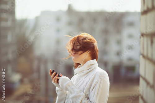 Young beautiful woman drinking tea on the balcony in a white sweater on a background of residential buildings. Still from the film.