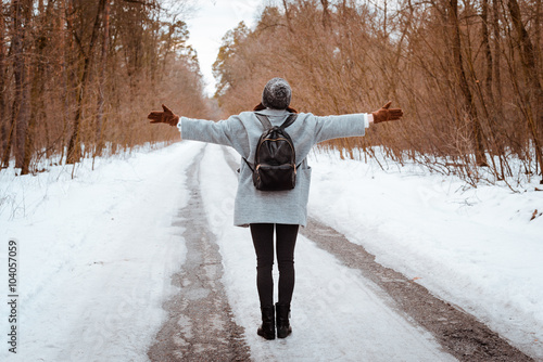 Portrait of a happy beautiful girl with brown hair in  winter forest.Attractive brunette woman dressed in a hipster style with black stylish leather backpack wearing grey coat and white pullover.