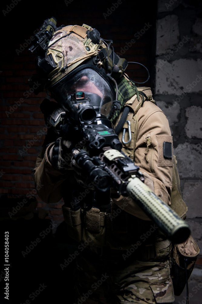 Soldier dressed in protective equipment, aiming at target.Selective focus/Soldier dressed in protective equipment as helmet and gas mask aiming at target from assault rifle.
