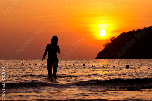 Young woman walking out of Andaman sea on sunset in Phuket island, Thailand