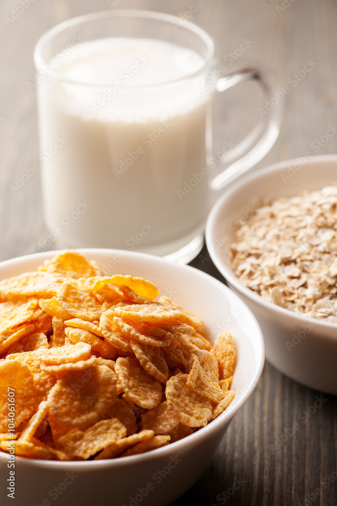 Cornflakes and oatmeal in white bowls with glass of milk Cornflakes and oatmeal in white bowls with glass of milk