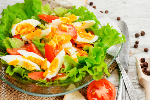  healthy salad with fresh vegetables , tomatoes , lettuce , boiled egg and spices and oil on a wooden background