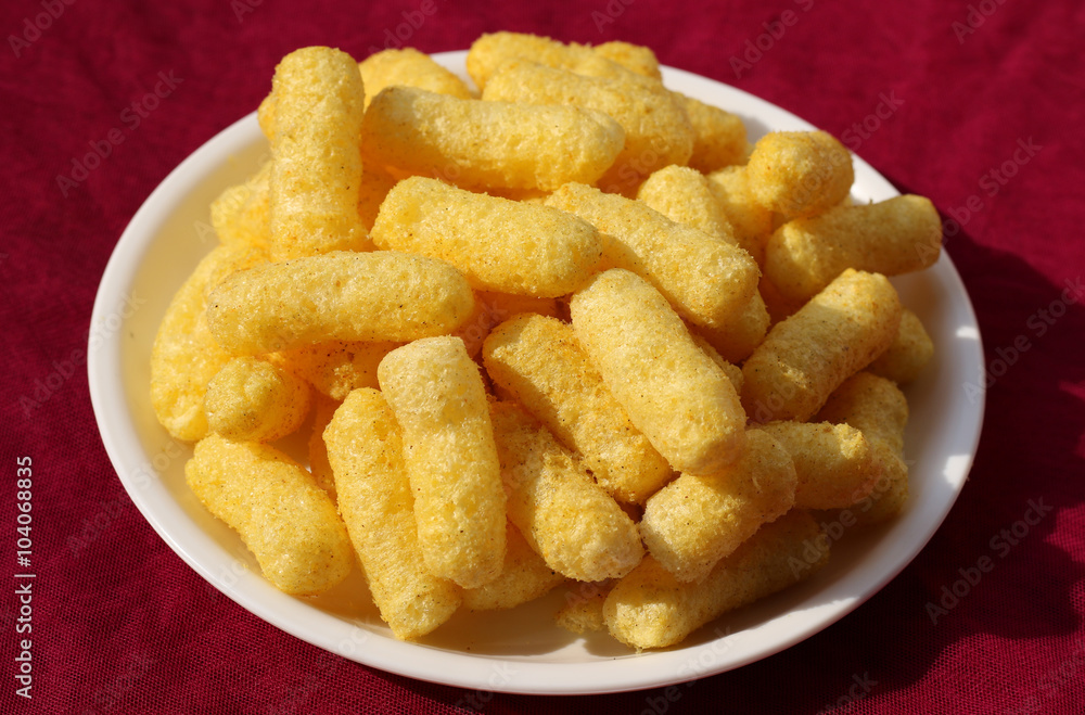 Crunchy corn puffs a tasty snacks in white pate on a red background Crunchy corn puffs a tasty snacks in white pate on a red background