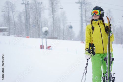 Female skier standing with skies in one hand on background beautiful mountain landscape