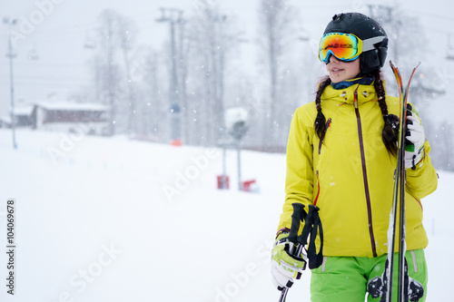 Female skier standing with skies in one hand on background beautiful mountain landscape