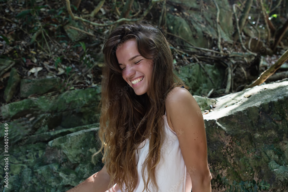 The beautiful fashionable girl with long hair, sits on surface kamnisto, dressed in a light white dress, finding on tropitechesky falls of the island Samui. Sunny day and happy smile. The beautiful fashionable girl with long hair, sits on surface kamnisto, dressed in a light white dress, finding on tropitechesky falls of the island Samui. Sunny day and happy smile.