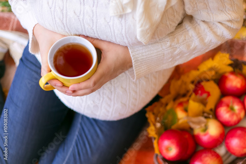 pregnant woman holding a cup of tea and sitting on the plaid in