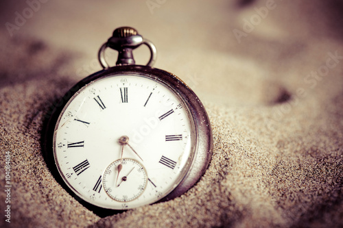 Gros plan sur une montre à gousset enterrée dans le sable avec filtre vintage