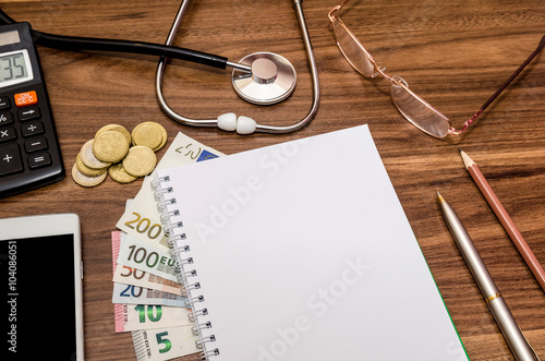 Φωτογραφία empry notepad with stethoscope, euro money, glasses, pen, calculator on table