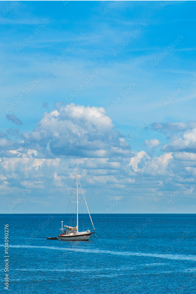 Isolated sailboat on blue ocean sea with white fluffy clouds in clear blue sky looking restful relaxing calm isolated secluded private