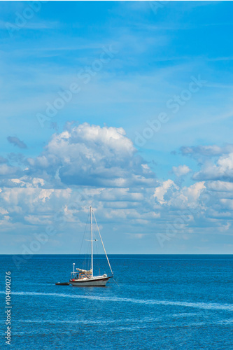 Isolated sailboat on blue ocean sea with white fluffy clouds in clear blue sky looking restful relaxing calm isolated secluded private