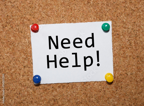 The phrase Need Help! typed on a white piece of note paper and pinned to a cork notice board