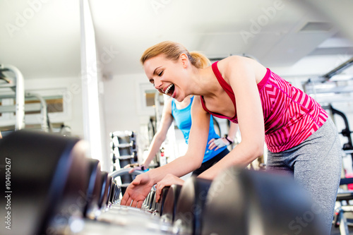 Detail of women in gym laughing, row of weights