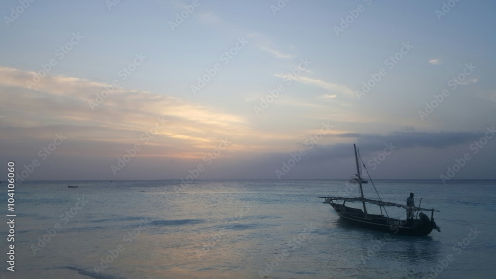 Traditional Dhow boat floating in the ocean as they he sun sets in Nungwi, Zanzibar Traditional Dhow boat floating in the ocean as they he sun sets in Nungwi, Zanzibar