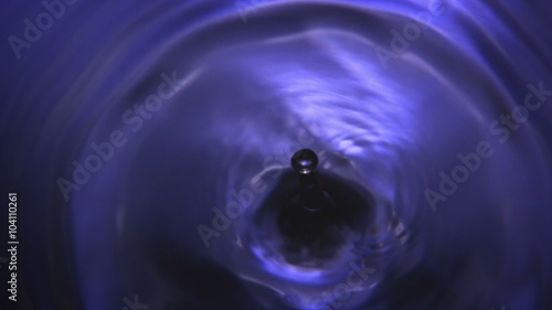 Purple Water Drop - A high quality, super slow motion in camera macro shot of a single violet water drop falling into frame, producing silky waves and ripple effects.