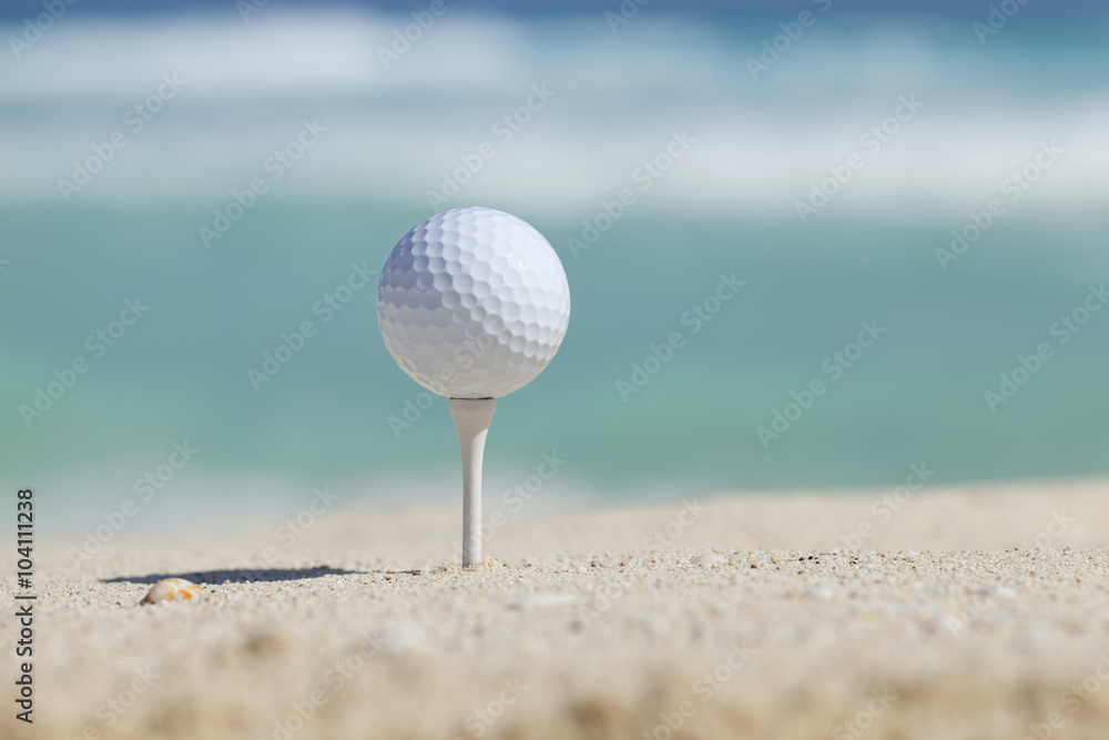 Golf ball on tee in sand beach with ocean waves behind Golf ball on tee in sand beach with ocean waves behind
