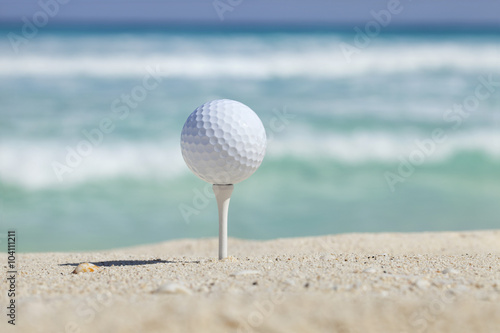Fototapeta Naklejka Na Ścianę i Meble -  Golf ball on tee in sand beach with ocean waves behind