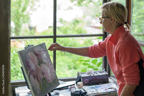 Женщина-художник рисует картину с букетом цветов маслом на фоне окна.