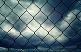 Outside wire fence closeup with dark dramatic cloudscape sky background.