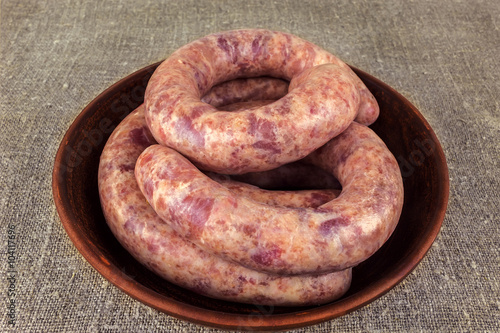 homemade sausage rings, raw meat in a clay plate on a burlap.