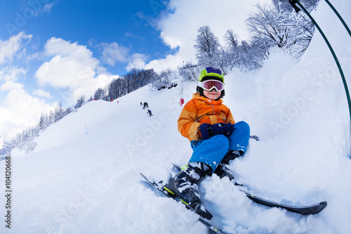 Child with ski and wearing mask sit in snow