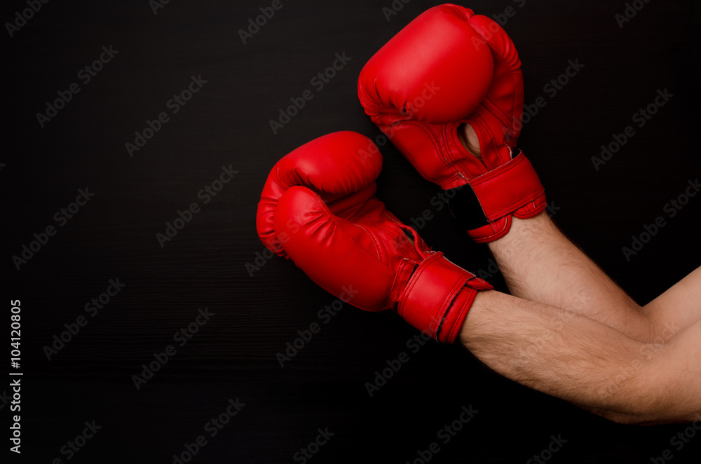 Hand in red boxing gloves in the corner of the frame on a black background, empty space