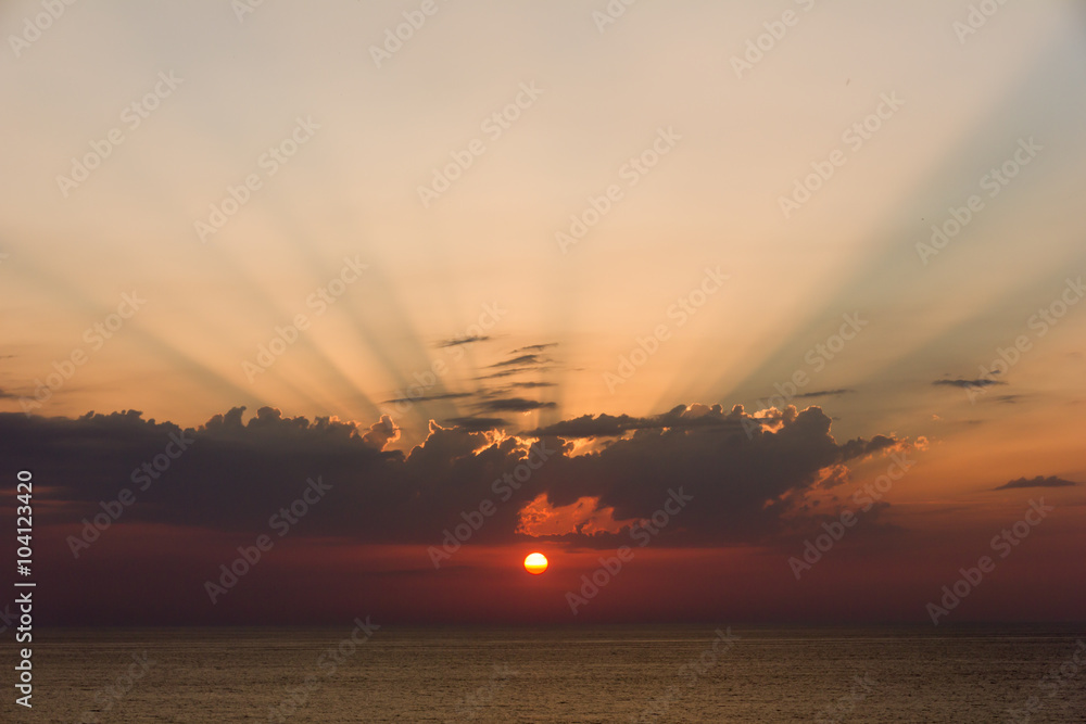 sunset over the ocean with visible sunshine over the clouds