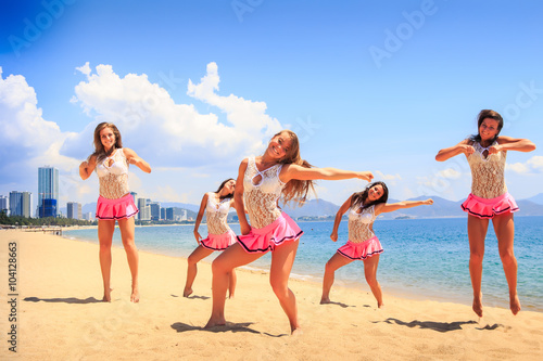 cheerleaders in dance pose hands aside on beach against sea