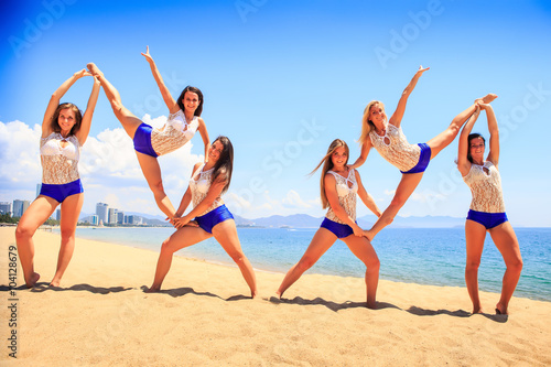 cheerleaders perform double Heel Stretch on sand against sea